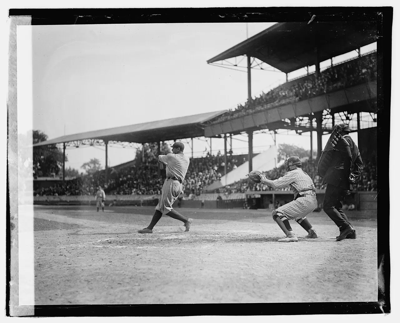 Babe Ruth swinging at a pitch with the catcher crouched behind him, 1920